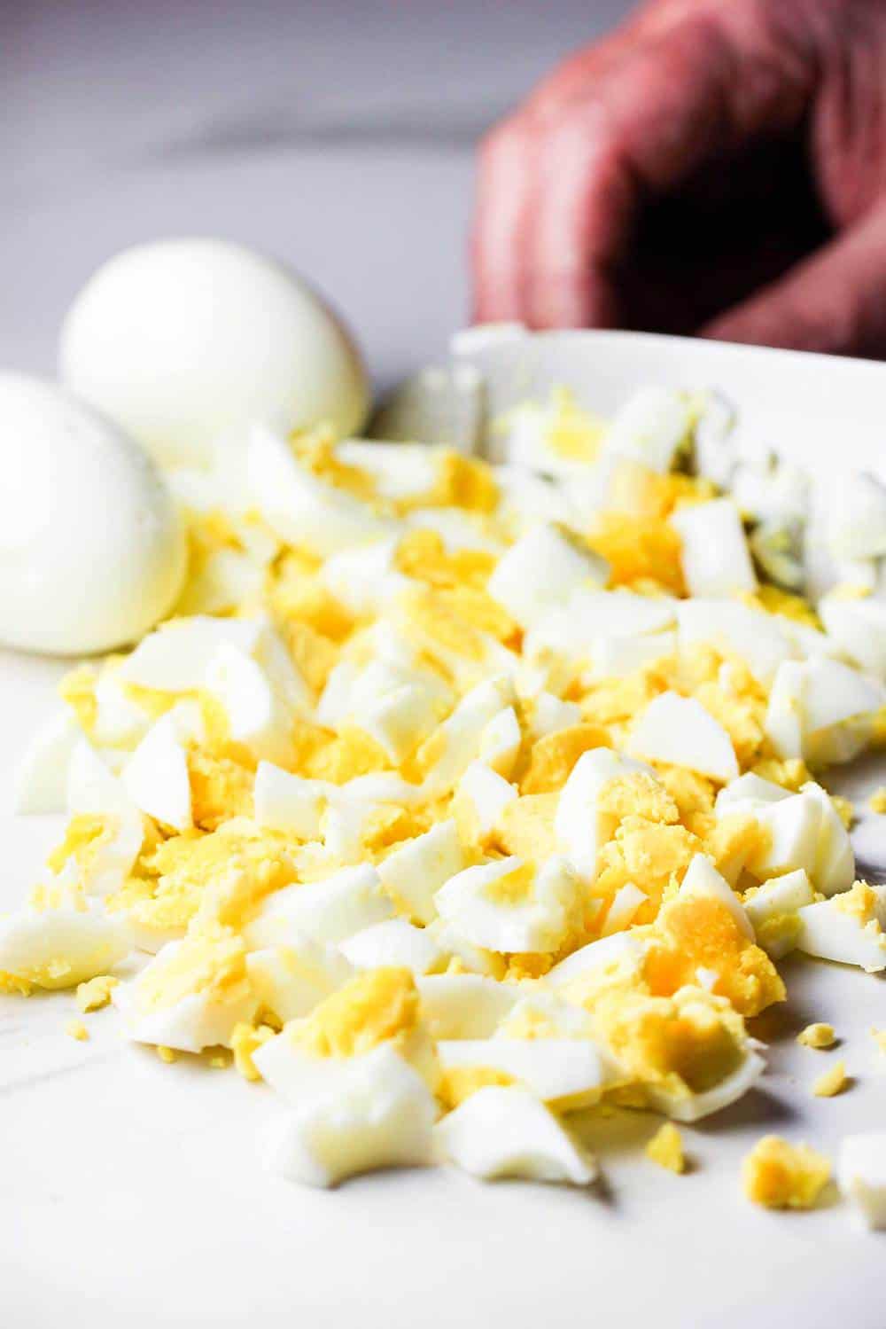 A chef's knife chopping cooked eggs for egg salad