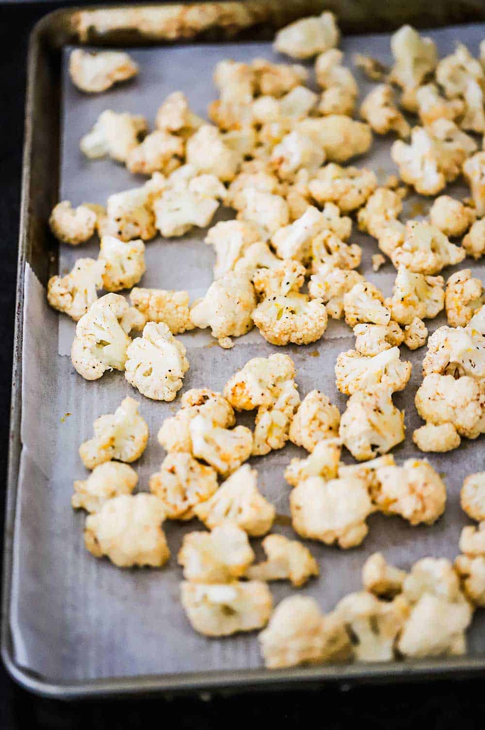 Seasoned cauliflower florets resting on a large baking sheet lined with parchment paper.