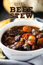 A white bowl filled with hearty beef stew next to torn white bread.