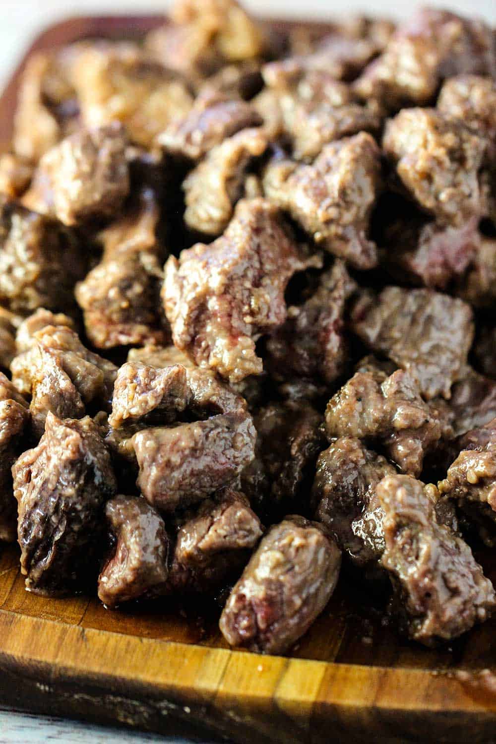 A pile of seared beef chuck on a wooden cutting board.