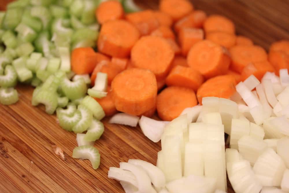 A wooden cutting board topped with sliced celery, carrots, and onion.