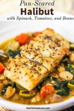A close-up view of a seared fillet of halibut sitting on top of sautéed spinach, tomatoes, olive, and beans all in a savory sauce.