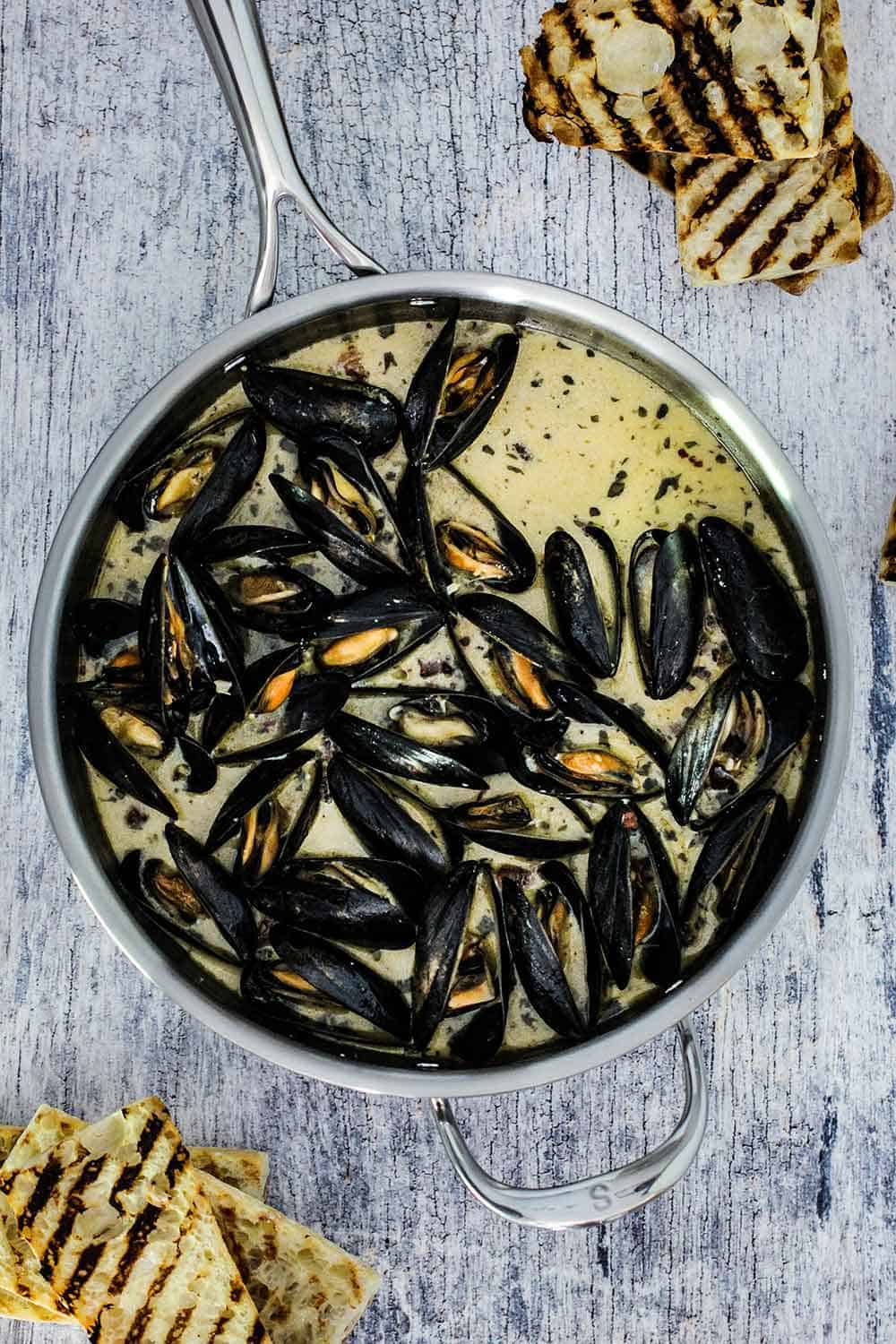 A large saucepan filled with steamed mussels with garlic and wine sauce.