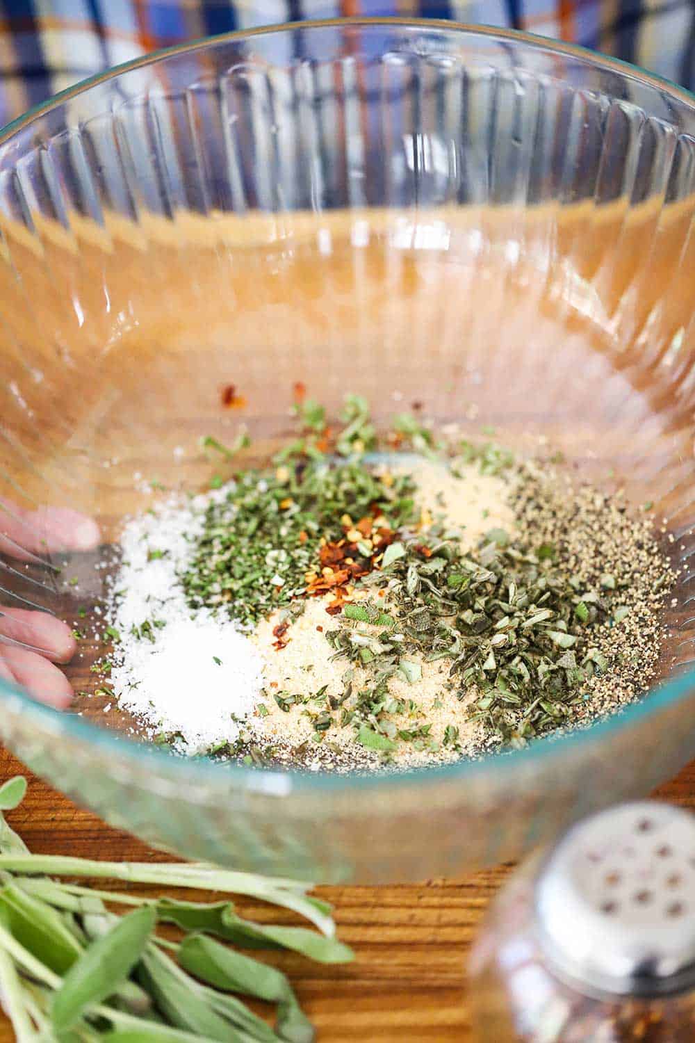 A large glass bowl filled with bread crumbs, fresh herbs, red pepper flakes, salt, and pepper.
