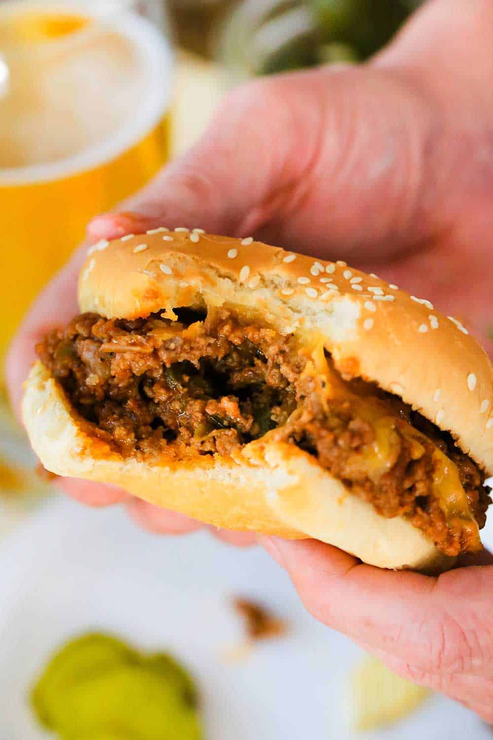 Two hands holding a sloppy joe sandwich with a bite taken out of it.