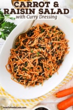 An overhead view of an oval white serving bowl filled with carrot and raisin salad with curry dressing.