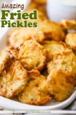 A rectangular platter filled with crispy fried pickles stack on top of each other.