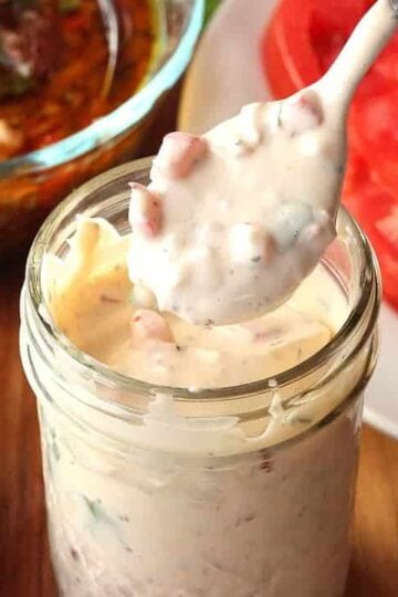 A jar of Chimichurri Mayonnaise sitting next to a plate of slice tomatoes.