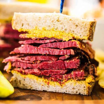 One half of a Wagyu pastrami sandwich sitting on a cutting board with the layers of meat exposed.