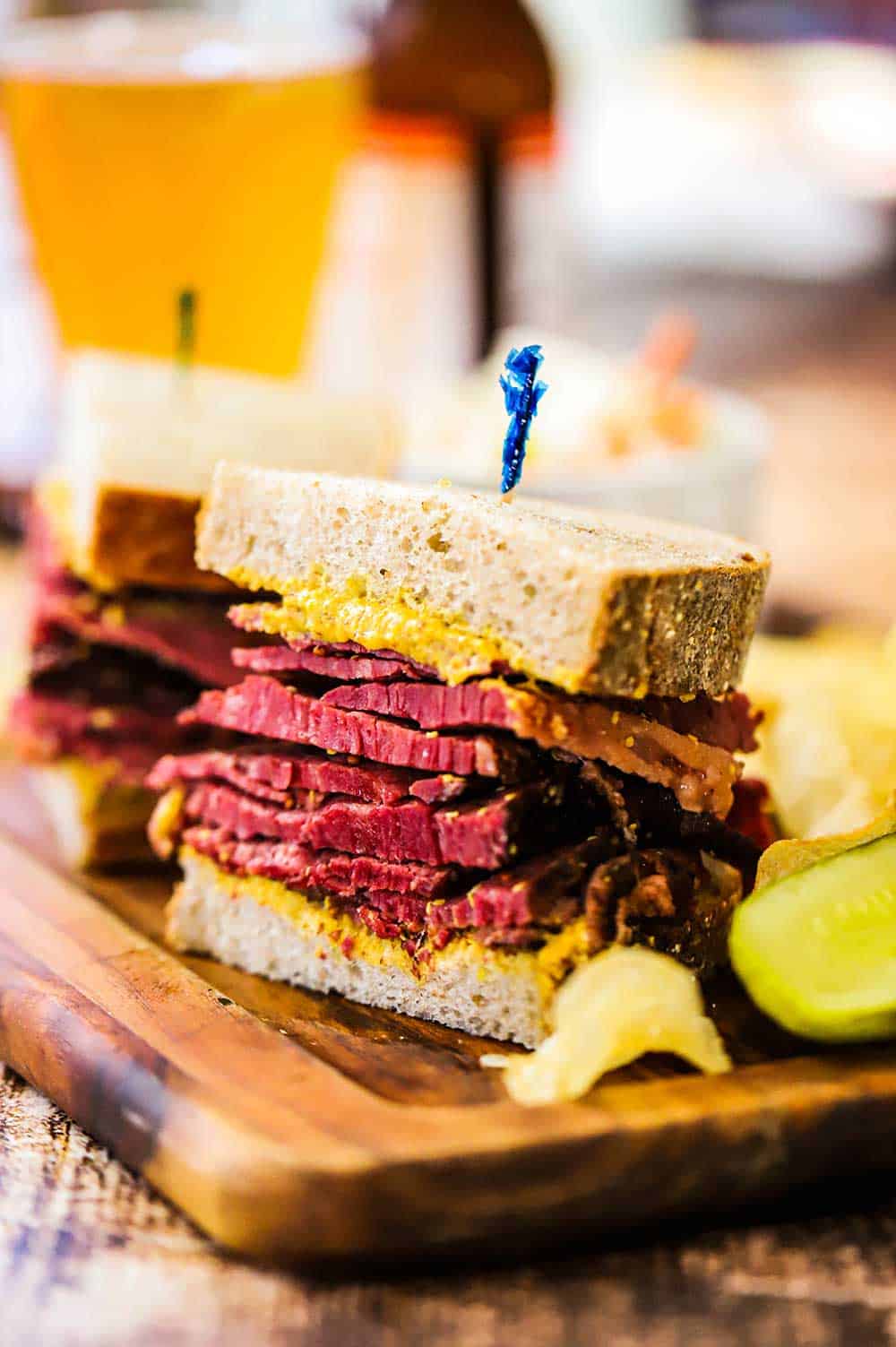 A pastrami sandwich that has been sliced into two halves both sitting a small wooden cutting board.