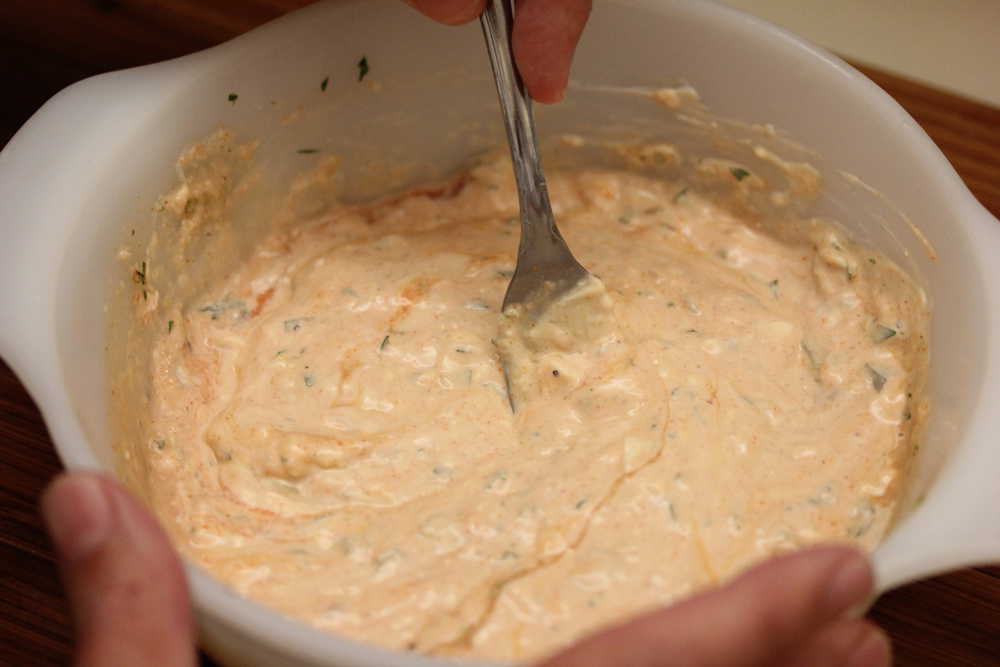 A fork mixing a white bowl filled with all the ingredients of Russian dressing.