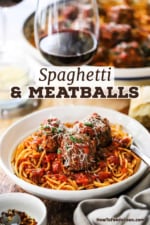 A close-up view of a white bowl filled with a serving of spaghetti and meatballs with parmesan cheese shredded over the top.