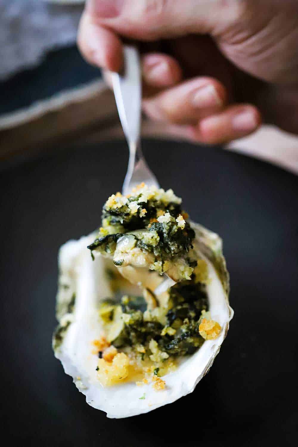 A spoon being held up with a spinach mixture in it from an oysters Rockefeller.