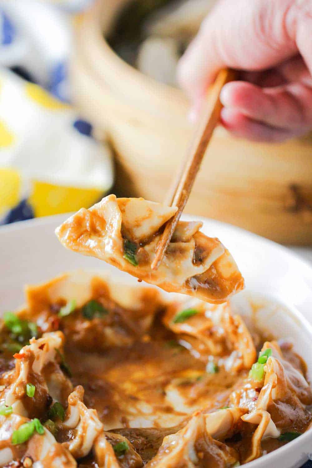 A pair of chop sticks holding up pork dumplings in a spicy peanut sauce.