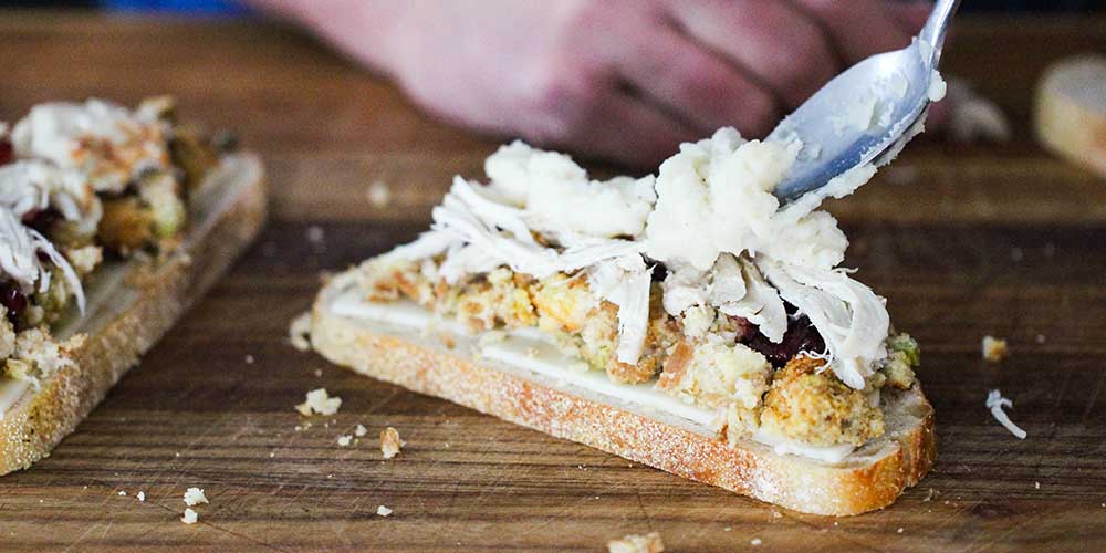 Mashed potatoes being added to a thanksgiving sandwich.