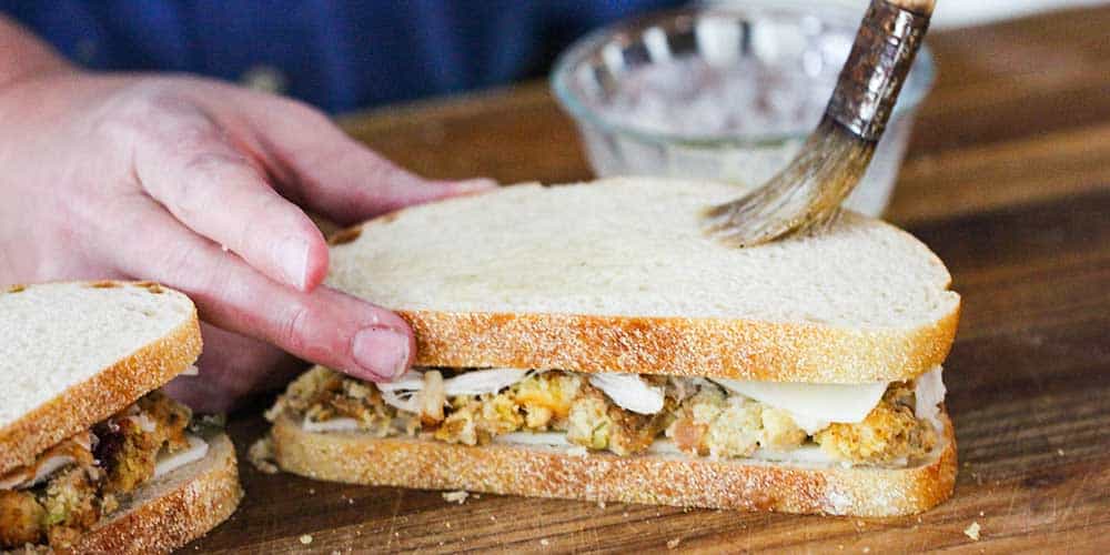 A hand brushing butter on to the top slice of bread on a day after Thanksgiving panini.