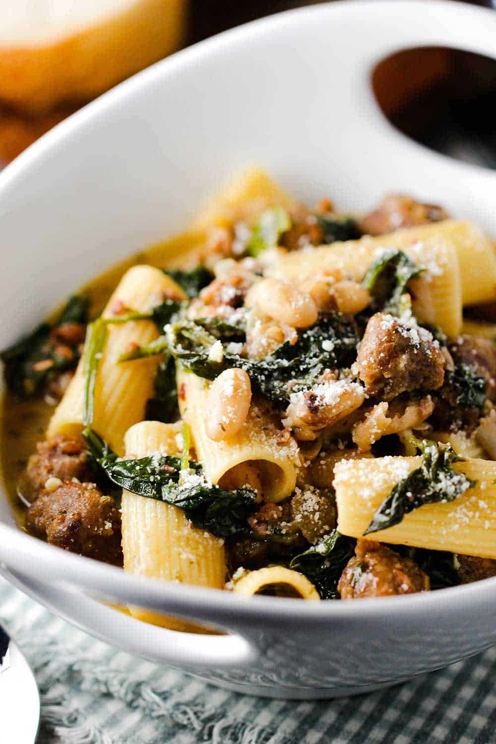 A close-up view of a white bowl holding country Italian pasta with sliced bread next to it.