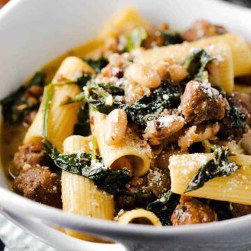 A close-up view of a white bowl holding country Italian pasta with sliced bread next to it.