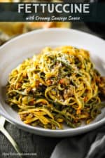A white individual serving bowl filled with fettuccine with creamy sausage sauce.