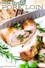 A chef's knife cutting into a herb-stuffed pork loin on a white platter.