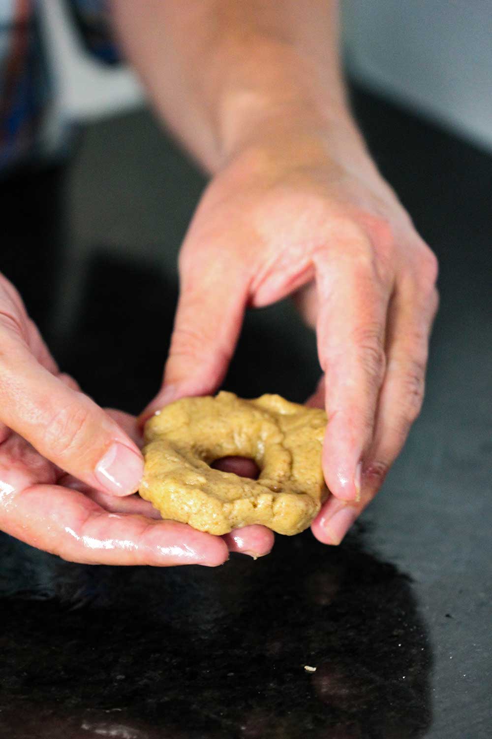 Two hands holding a doughnut shaped piece of batter for apple cider doughnuts.