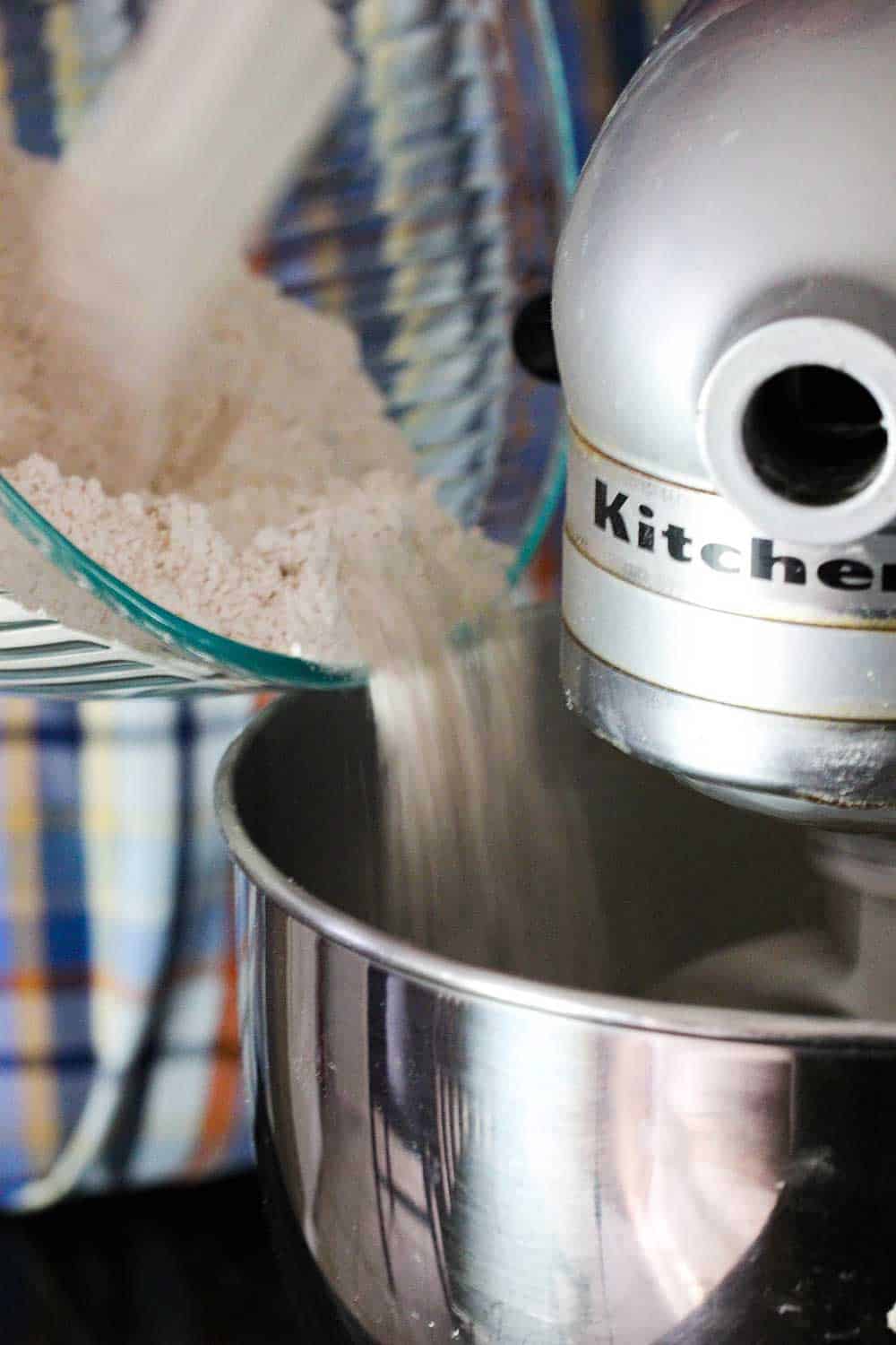 A bowl of flour and cinnamon being poured from into a large stand mixer for apple cider doughnuts.