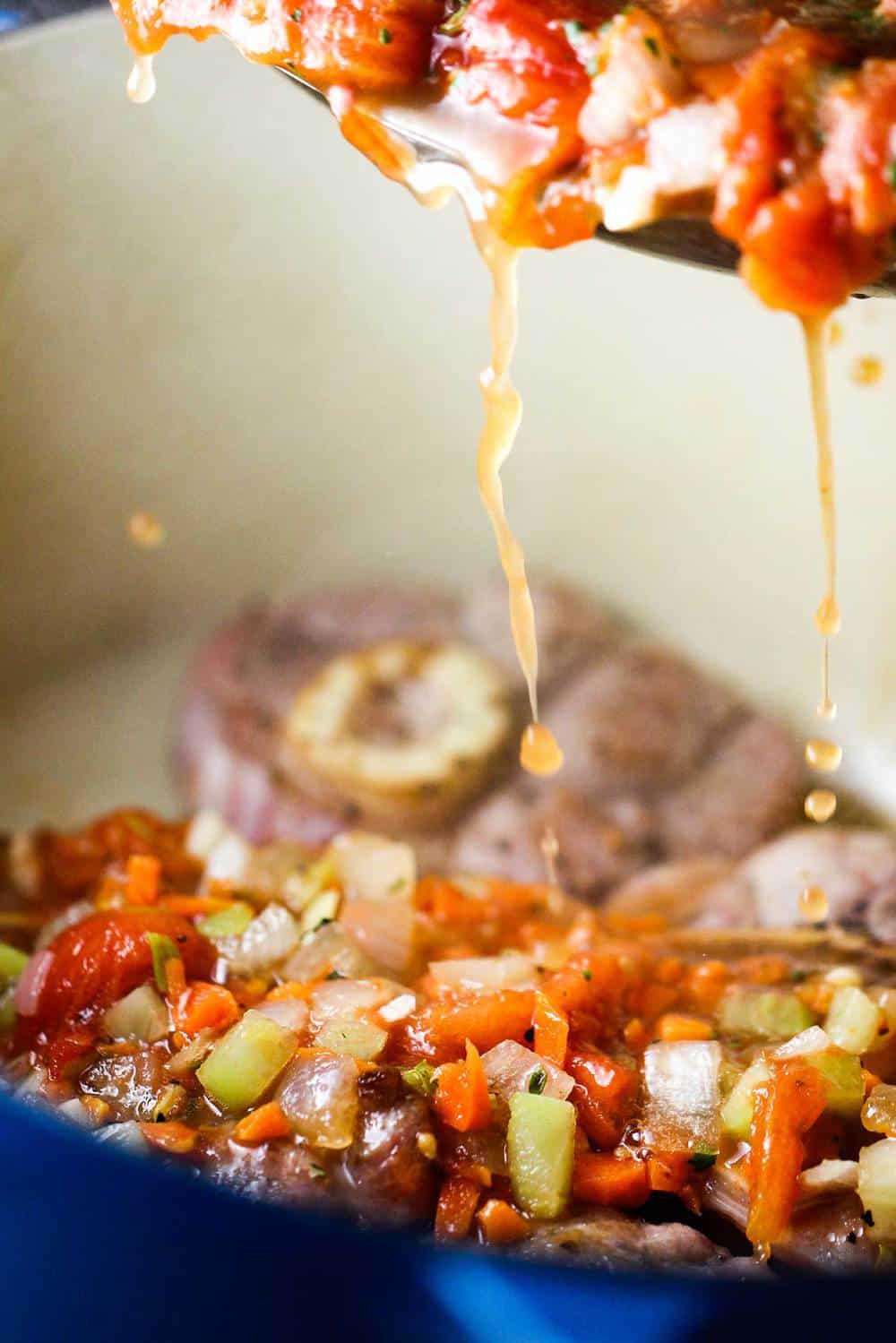 Sautéed vegetables and stock pouring over veal shanks