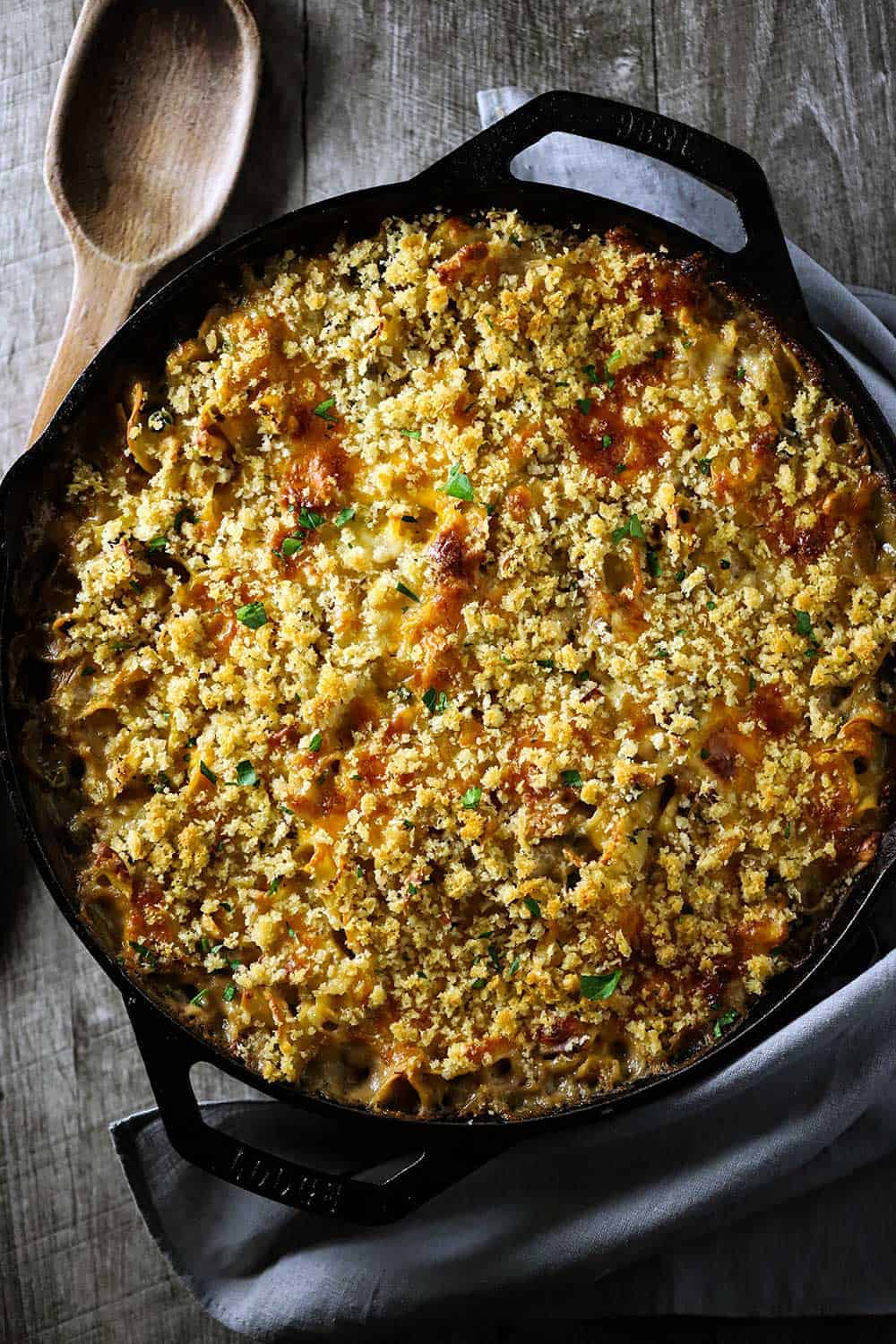 A white bowl holding a large serving of Gourmet Tuna Casserole next to a yellow casserole dish full of the same casserole.
