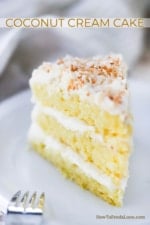 A 3-layered slice of coconut cream cake on a white dessert plate.