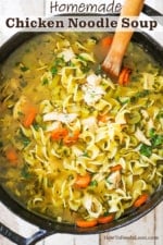 A black pot with handles filled with homemade chicken noodle soup topped with chopped fresh parsley.