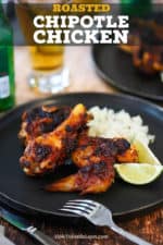 A black dinner plate filled with two pieces of roasted chipotle chicken, cilantro-lime rice, and 2 lime wedges, all sitting next to a glass of Mexican beer.