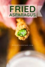 A hand holding a fried asparagus stalk that has been bitten in half.