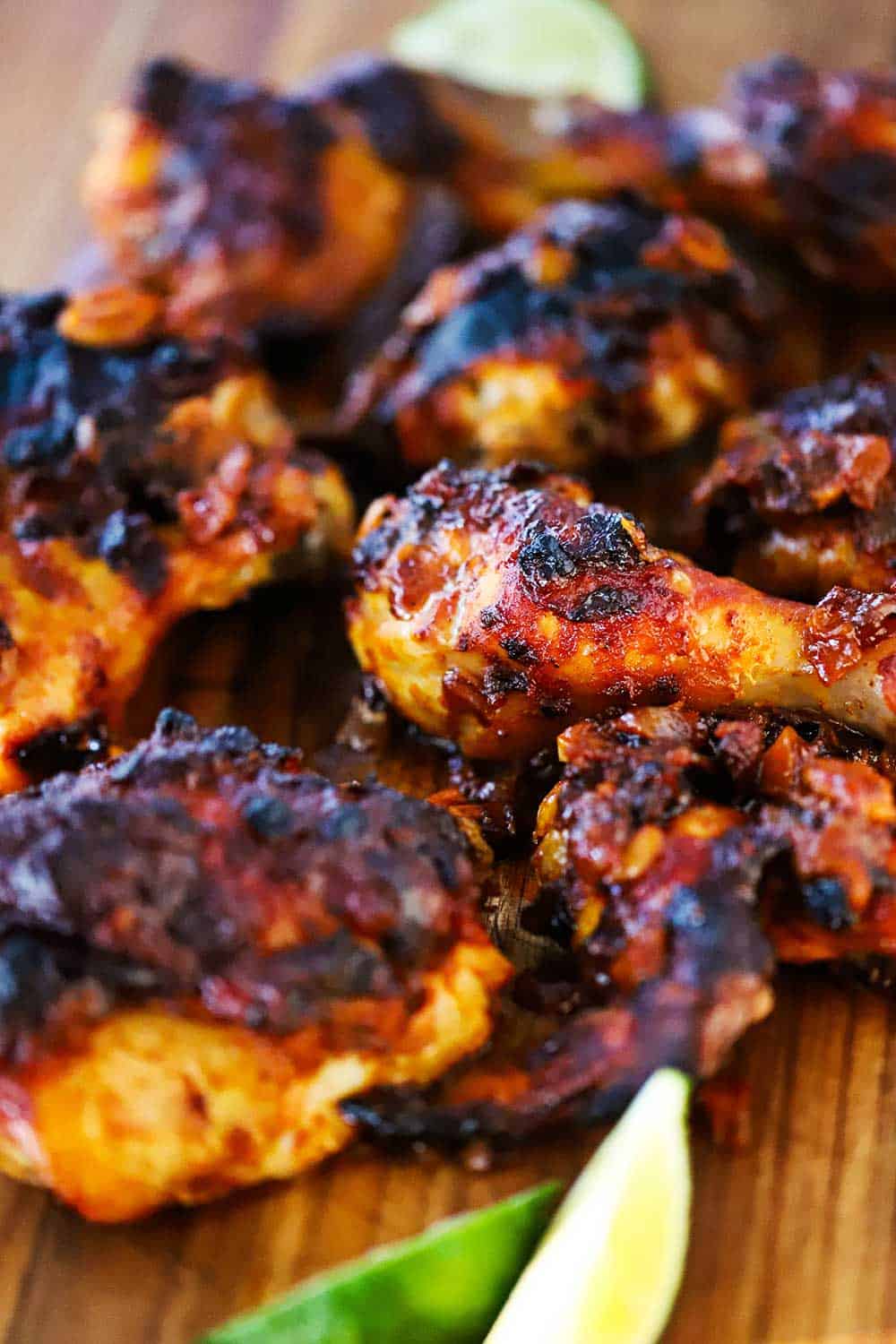 A large wooden cutting board topped with numerous pieces of roasted chipotle chicken next to 2 lime wedges.