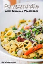 A large white serving bowl filled with fresh pappardelle pasta and sautéd spring vegetables.