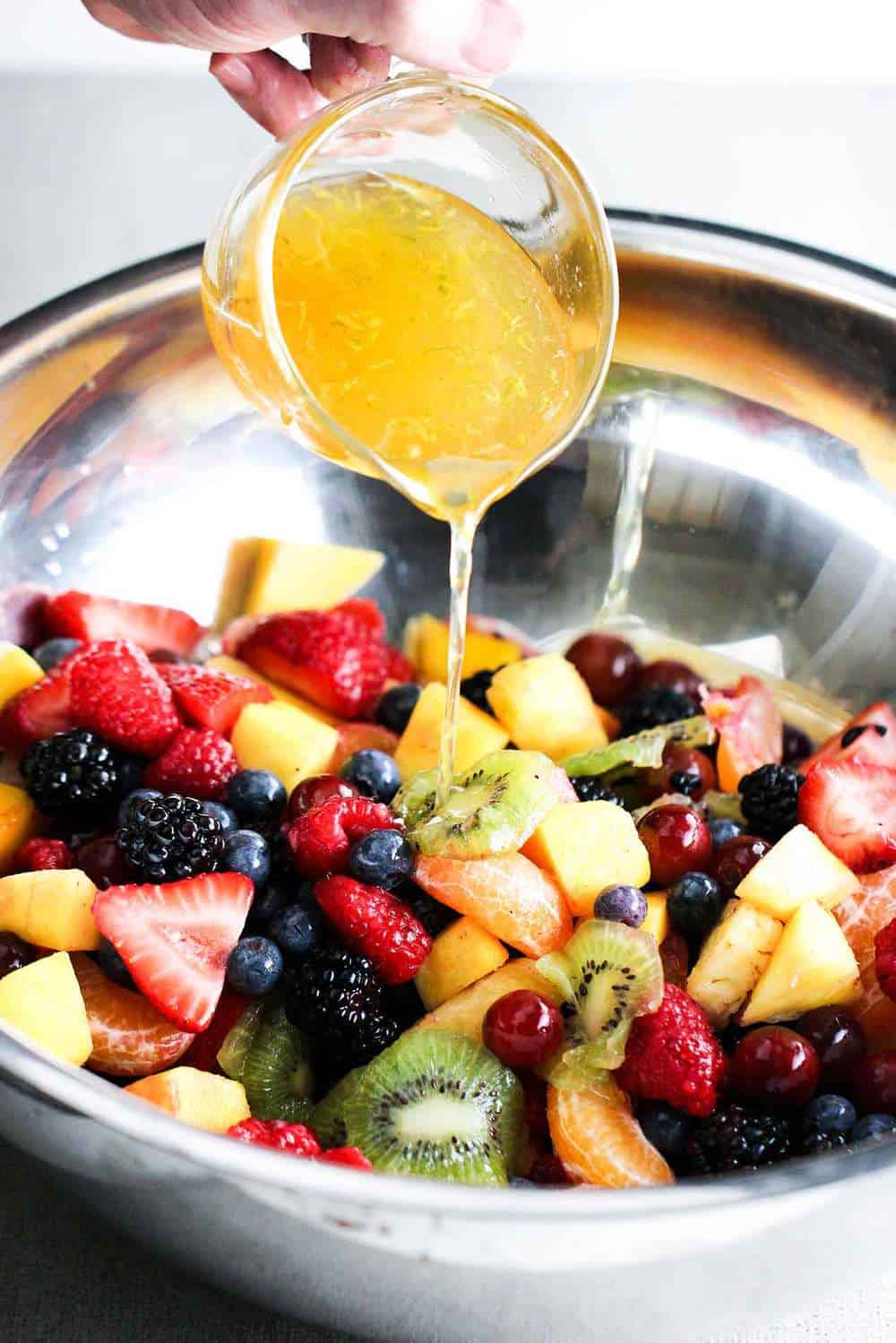 Dressing pouring onto a bowl of fruit for summer fruit salad.