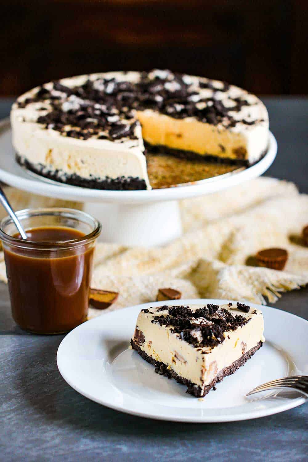 Place a slice of peanut butter cup ice cream cake on a small white plate next to caramel sauce.