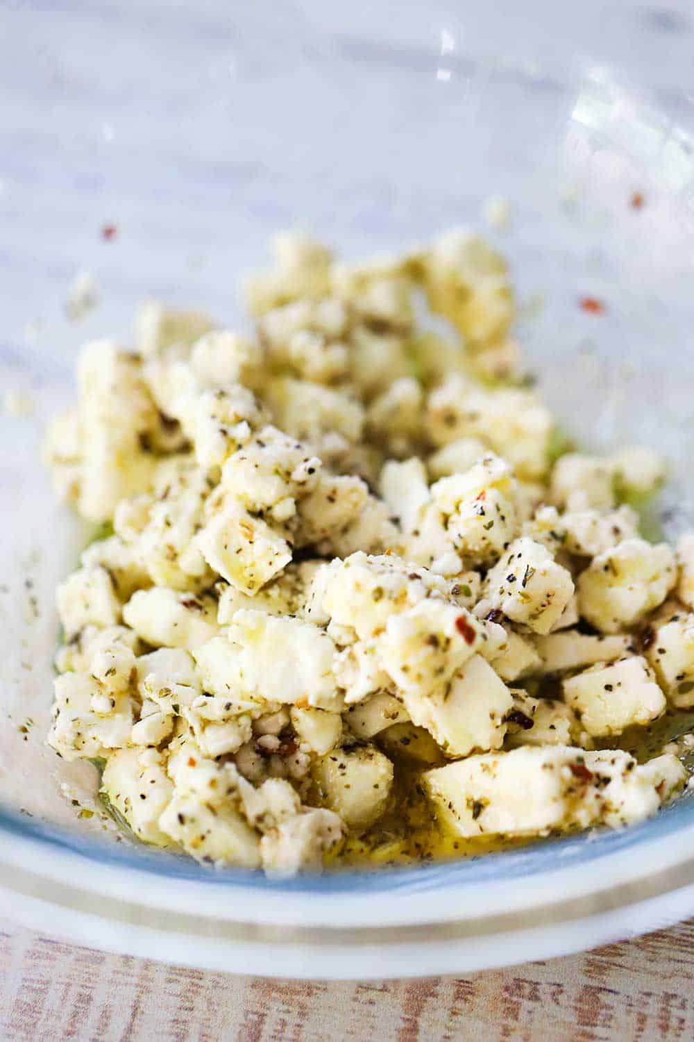 A glass bowl filled with crumbled marinated feta cheese.
