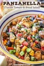A straight-on view of a large serving pasta bowl filled with panzanella that has been topped with shaved Parmesan cheese.