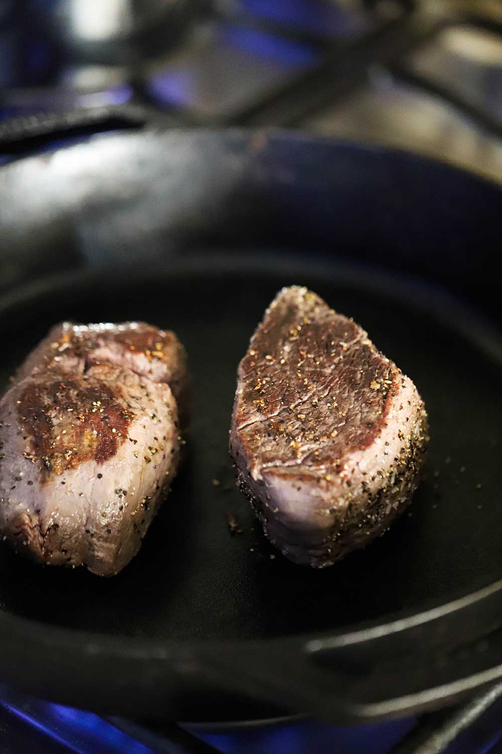 Two beef tenderloin steaks that have been seared and are sitting in a large cast-iron skillet.