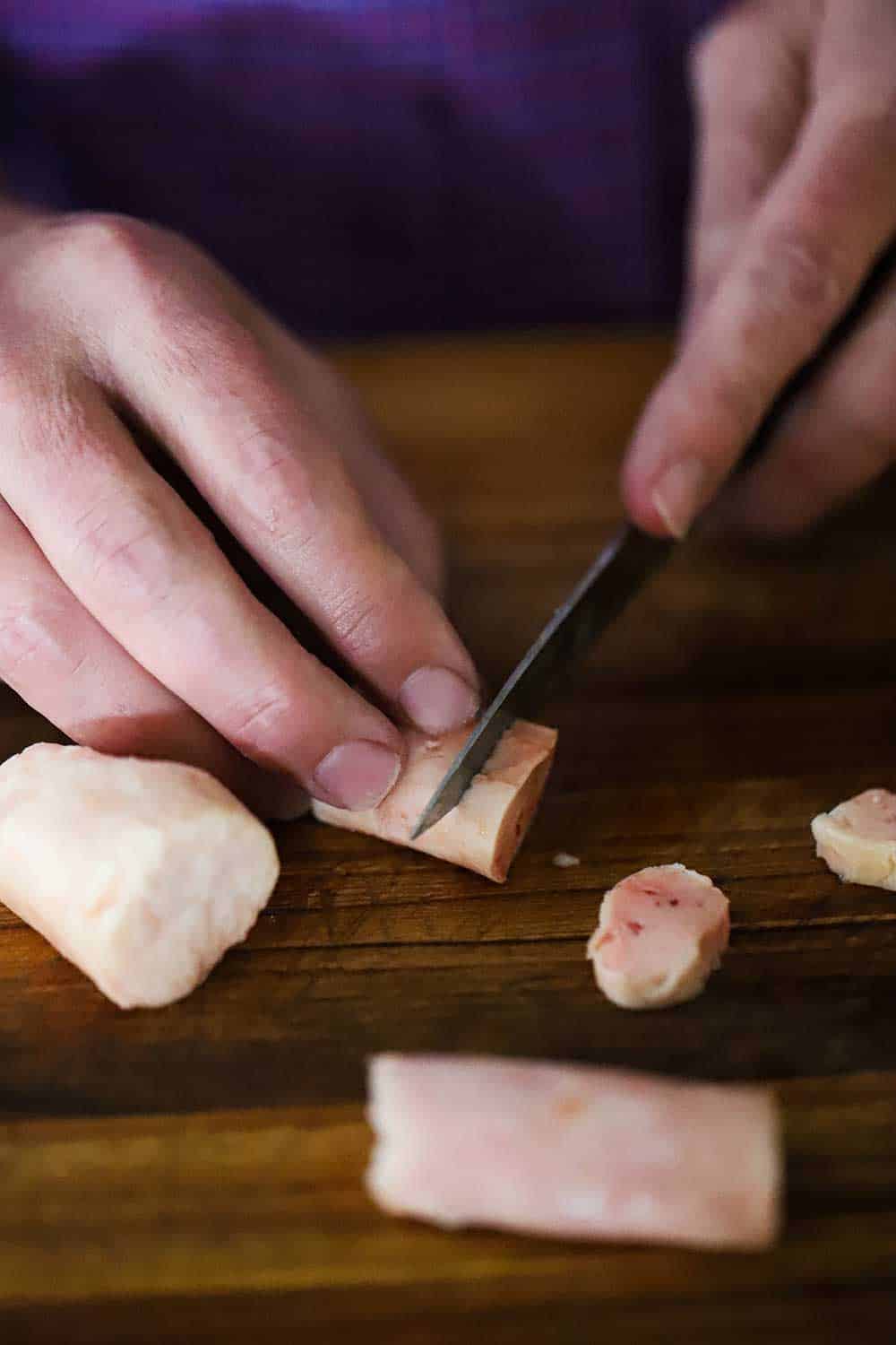 A person using a small knife to slice small medallions from a 2-inch long piece of beef bone marrow.