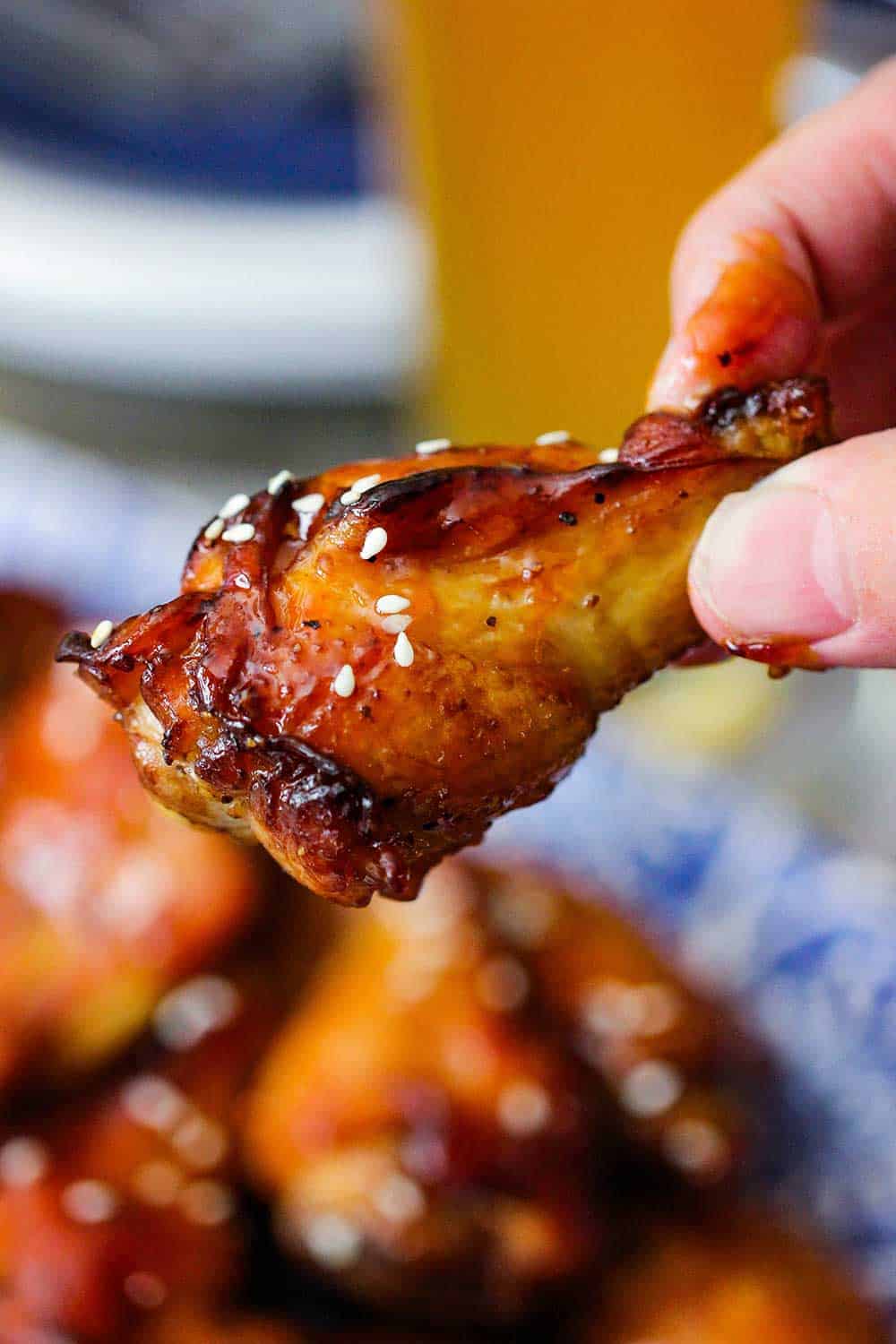 A hand holding a baked chicken wing with sesame seeds on it.