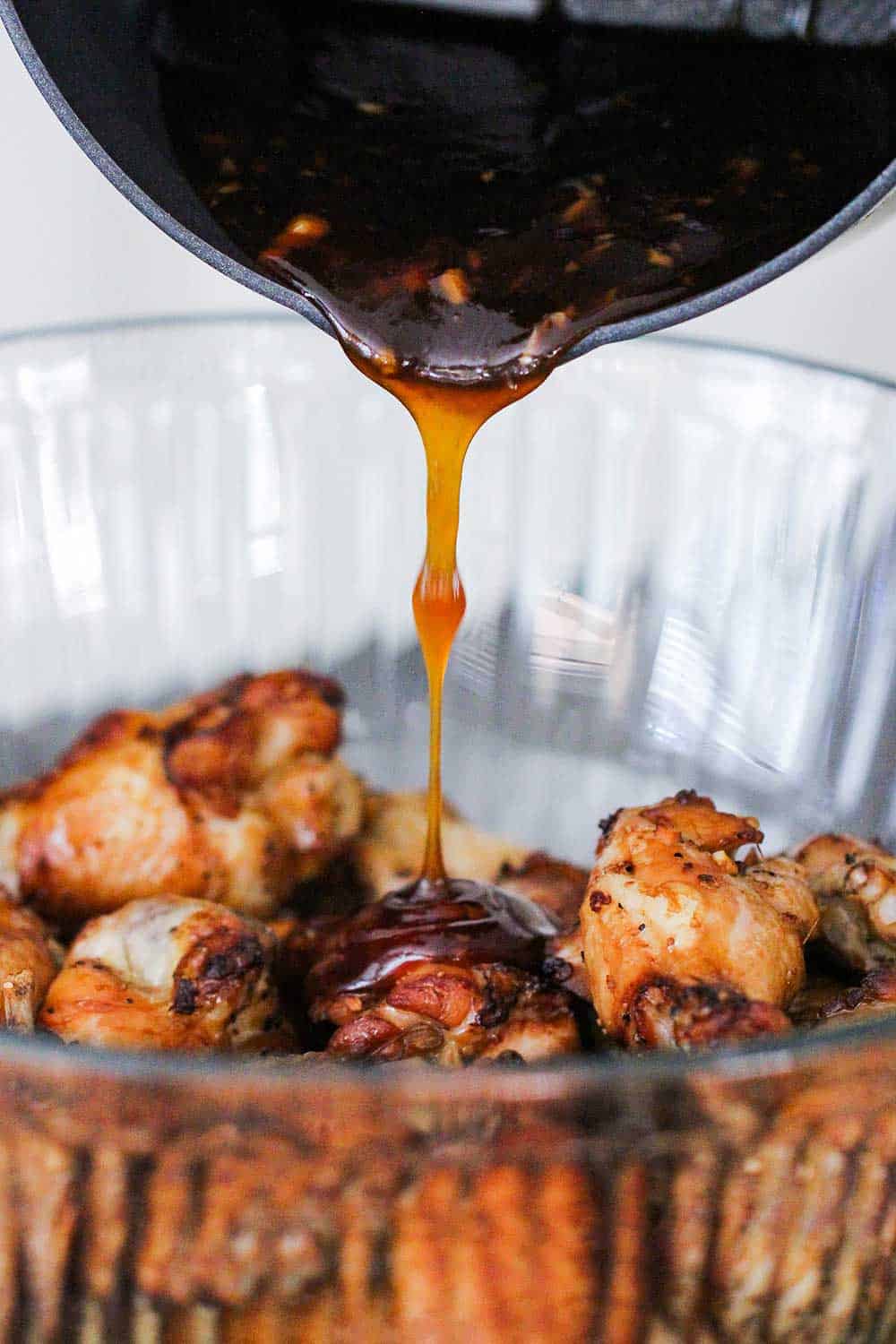 A sauce pan pouring teriyaki sauce over baked chicken wings.