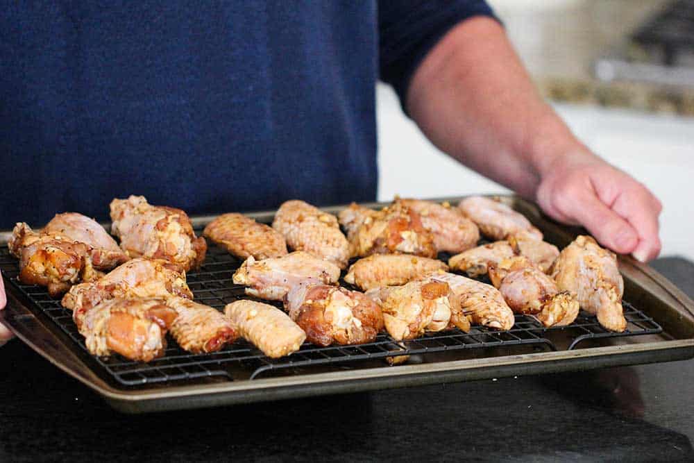 Two hands holding a baking rack on a baking sheet filled with uncooked teriyaki chicken wings.