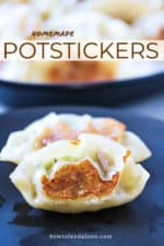 Two cooked potstickers sitting on a black plate with a platter of potstickers in the background.