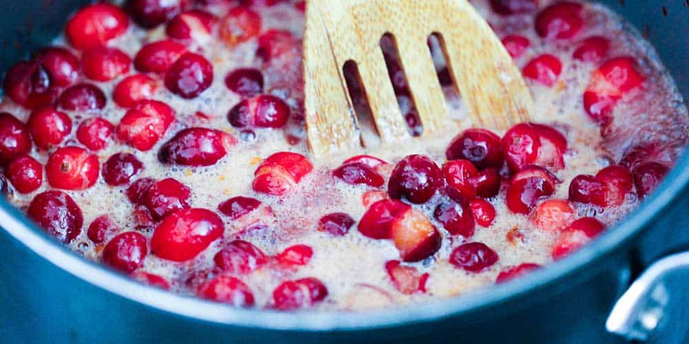 A pan of simmering cranberries with a wooden spoon in it.