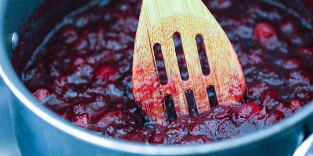 A wooden spoon in a pan of maple orange cranberry sauce.
