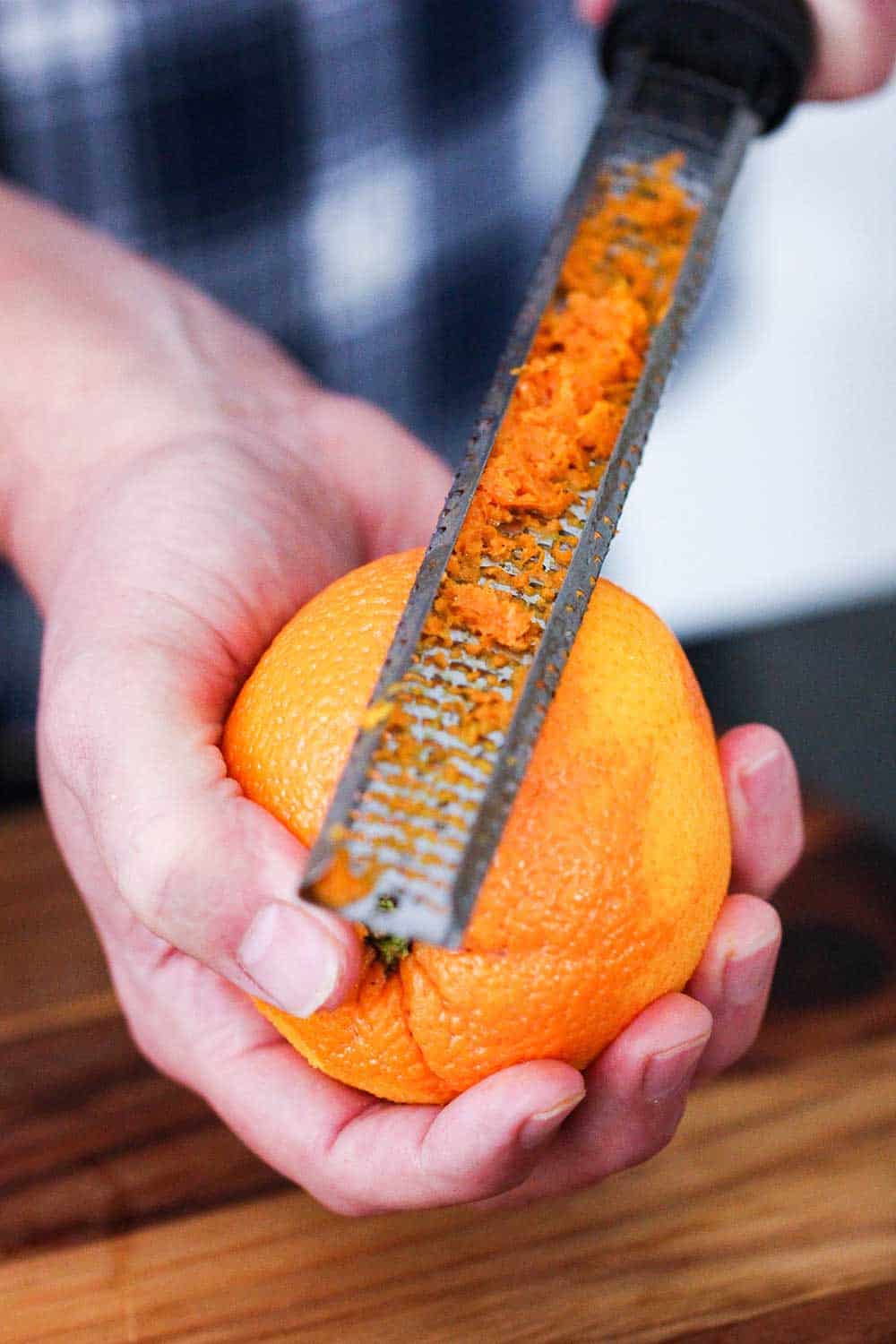 One hand holding an orange while the other hand is use a zester to zest the orange.