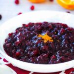 A white bowl containing homemade cranberry sauce with a sliced orange next to it.