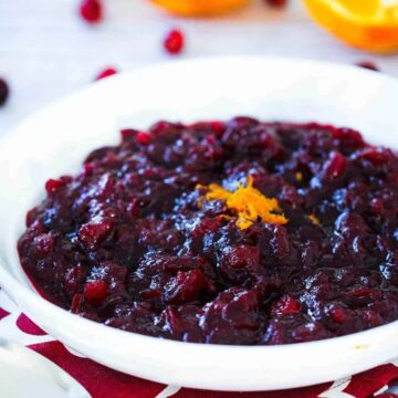 A white bowl containing homemade cranberry sauce with a sliced orange next to it.