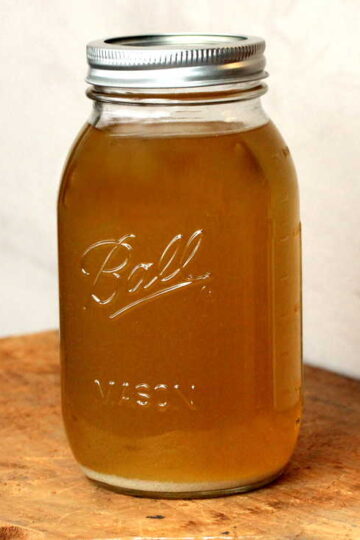 A large jar holding seafood stock on a wooden table.